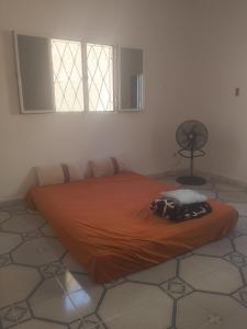 ein Bett mit einer orangefarbenen Decke in einem Zimmer mit einem Ventilator in der Unterkunft Dar Daoudi in Nouakchott