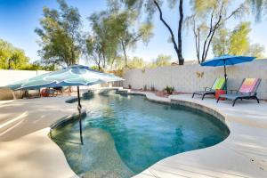 uma piscina com um guarda-sol e duas cadeiras em Charming Gilbert Home with Patio and Putting Green! em Queen Creek