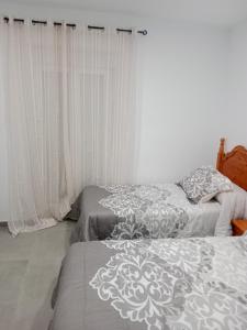 2 camas en un dormitorio con cortinas blancas en Apartamentos los carros 2 en Guadix
