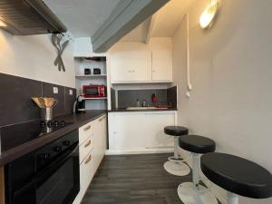 a kitchen with white cabinets and black counters and stools at L'appartement Marceau - 55m2 - Carcassonne centre in Carcassonne