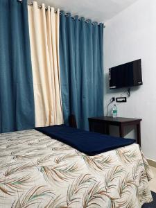 a bedroom with a bed with blue curtains and a television at Puthookadans Mareena Lodge in Kottayam