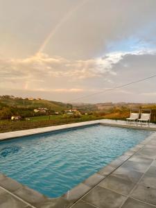 a pool with two chairs and a rainbow in the background at Tenuta Agricola La Cava- Cantina e Agriturismo in San Damiano dʼAsti