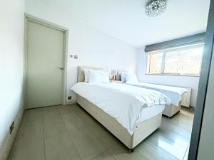 a white bedroom with two beds and a window at Peacock Court in London