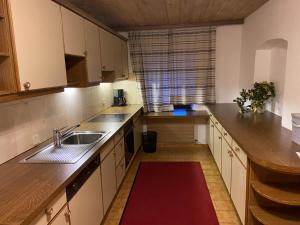 una cocina con armarios blancos, fregadero y alfombra roja en Appartment Thumerhof Wildschönau en Niederau