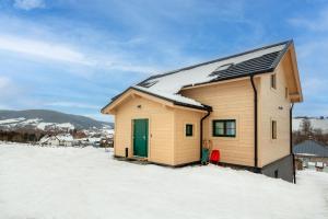 une petite maison avec une porte verte dans la neige dans l'établissement Apartamenty Dubacik, à Tylicz