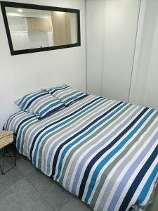 a bed with a blue and white striped comforter and a mirror at Appartement dans maison atypique in Montrond-les-Bains