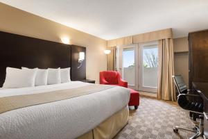 a hotel room with a bed and a red chair at Days Inn & Suites by Wyndham North Bay Downtown in North Bay