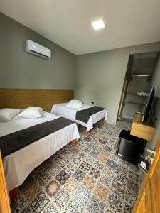 a hotel room with two beds and a television at Santa Clara Pousada in Guarujá