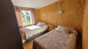 two beds in a small room with a window at Cabaña Pradera Premiun I in Llau-Llao