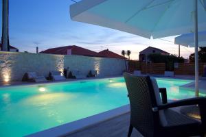 a swimming pool with a chair and an umbrella at Banić Apartments with pool in Biograd na Moru