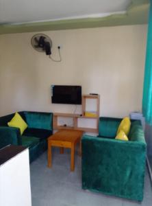 sala de estar con 2 sofás verdes y TV en MAGNOLIA SUITES, en Ukunda