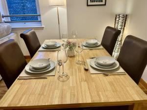 a wooden table with chairs and plates and wine glasses at La Scala Inverness City Apartment in Inverness