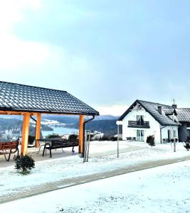 a pavilion with benches and a building in the snow at ,,KICZARA" Pokoje Na Punkcie Widokowym w Polańczyku z widokiem na Jezioro Solińskie i góry---601--806--454--- in Polańczyk