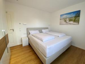 - un lit blanc dans une chambre avec une photo sur le mur dans l'établissement Wilde Brise - Ihr Luxusbungalow in Norddeich, à Norddeich