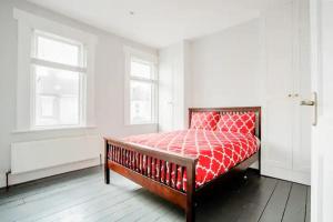 a bedroom with a bed with a red comforter and two windows at Spacious Stratford house in London