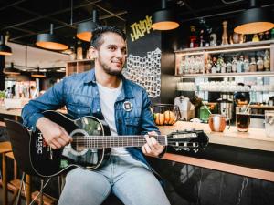 Um homem sentado num bar a tocar guitarra. em ibis Paris Bercy Village em Paris