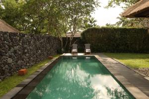 a swimming pool with two chairs next to a wall at Alila Ubud in Ubud