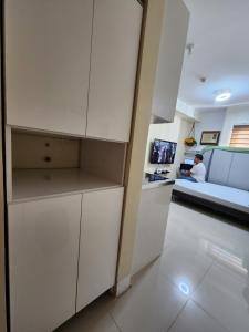 a kitchen with white cabinets and a man sitting on a couch at Budget price condo near IT Park & Ayala, Cebu City in Cebu City