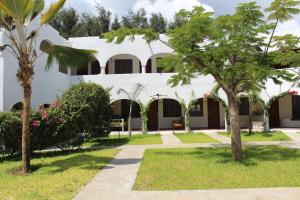 un edificio blanco con árboles en el patio en Kaleb's Beachfront Serviced Studio Apartments, en Malindi