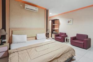 a bedroom with a bed and two purple chairs at Collection O 93163 Hotel Grand Kartika in Parepare