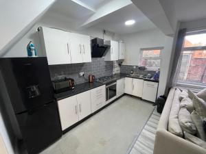 eine Küche mit weißen Schränken und einem schwarzen Kühlschrank in der Unterkunft Spacious 4-Bedroom House in Manchester in Manchester