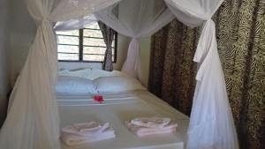 a bed with white curtains and towels on it at Les Datchi Cottages in Diani Beach