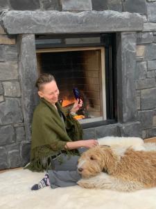 a man sitting next to a dog in front of a fireplace at Romantic Luxury Retreat with Private Sauna & Spa, Pet Friendly, Elkside Hideout B&B in Canmore