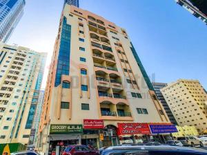 un edificio alto con coches estacionados frente a él en Masat El Sharjah for men, en Sharjah