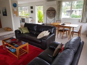 ein Wohnzimmer mit einem schwarzen Ledersofa und einem Tisch in der Unterkunft TayFord Cottage in Waipu