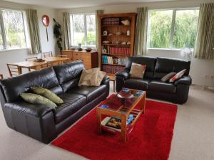 a living room with two leather couches and a red rug at TayFord Cottage in Waipu