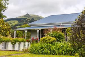 ein weißes Haus mit einem Zaun und Bergen im Hintergrund in der Unterkunft Halfmoon Cottage in Akaroa