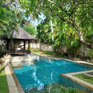 einen Pool in einem Garten mit Pavillon in der Unterkunft The Royal Beach Seminyak Bali in Seminyak