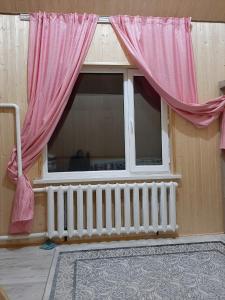 a window with pink curtains in a room with a radiator at Eldos_Kolsai in Saty