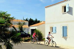 twee mensen die fietsen in een straat naast een gebouw bij Résidence Goélia La Palmeraie in Saint-Georges-dʼOléron