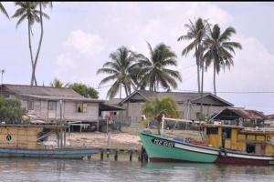 a boat sitting on the water near a house at D Landai Budget Room Family in Pekan