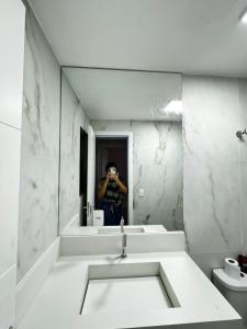 un uomo che scatta una foto a uno specchio del bagno di Apart Verdemar Confort com 3 quartos para ate 8 pessoas moderno e funcional e apenas poucos passos da praia a Maceió