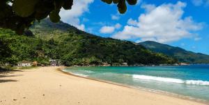 a beach with the ocean and mountains in the background at Suite Baia dos Corais in Angra dos Reis