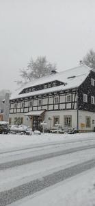 Un grand bâtiment blanc avec de la neige au sol dans l'établissement Gasthof Alte Schmiede G*** Lückendorf, à Luftkurort Lückendorf