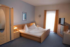 Schlafzimmer mit einem Bett mit weißer Bettwäsche und einem TV in der Unterkunft Hotel-Restaurant Christine in Lübz