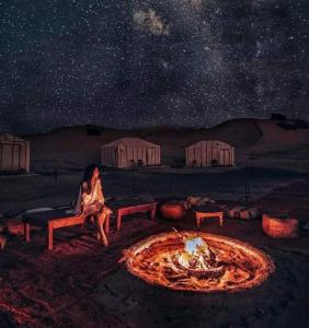 una mujer sentada al lado de un pozo de fuego por la noche en كعب غزال, en Merzouga