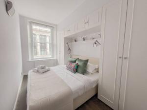 a white bedroom with a large bed with green pillows at Exceptional apartment in the most desirable street in London