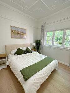 a white bedroom with a large bed with green pillows at three bedroom house within walking distance to light rail station in Sydney