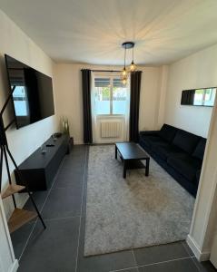 ein Wohnzimmer mit einem schwarzen Sofa und einem Tisch in der Unterkunft Duplex avec extérieur privatif proche Paris/CDG in Livry-Gargan