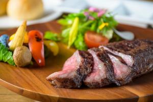 un pezzo di bistecca su un piatto di legno con verdure di Hotel Edel Warme a Furano