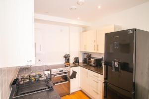 a kitchen with a black refrigerator and white cabinets at Cosy 1Bedroom Apartment in Greenwich Cutty Sark in London