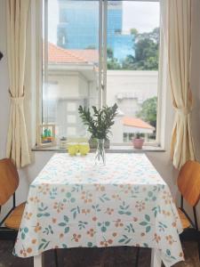 a table with a table cloth with a vase on it in a window at The Nest Homestay in Ho Chi Minh City