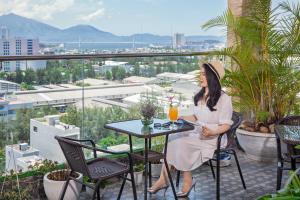 a woman sitting at a table on a balcony with a drink at Bliss Luxury Hotel & Spa in Da Nang