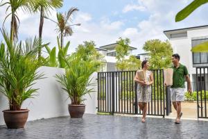 a man and a woman walking through a gate in front of a house at Friendly Townhouse Laguna Park in Thalang