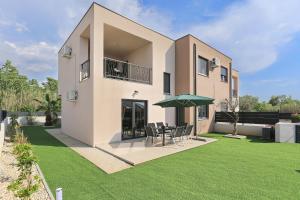 ein Haus mit einer Liegewiese mit einem Tisch und einem Sonnenschirm in der Unterkunft Villa Tri Palme with heated pool in Vrsi