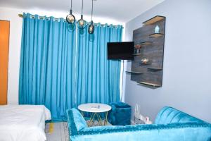 ナイロビにあるAqua Modern Studio Near Ngong Roadの青いカーテン、ベッド1台、テーブルが備わる客室です。